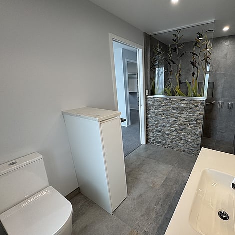 Image of tiled floor bathroom with stone edged shower wall in Te Wharepu Road new home build. Built by Ardent Building Developments, Hamilton. Waikato, New Zealand.