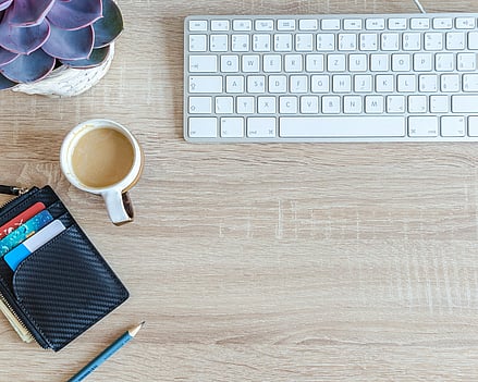 Keyboard, coffee and wallet on an oak desk.