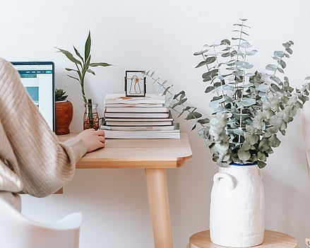 Virtual assistant working at her laptop on her desk. Books and plant to her right.