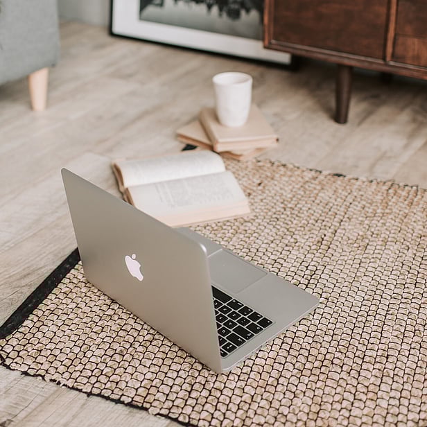 Laptop and books sitting open on the floor on top of reed carpet.
