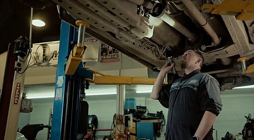 A mechanic looking at the underbody of a vehicle.