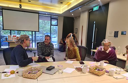 Small group discussion at workshop table with notebooks, snacks and drinks, people talking in meeting room setting