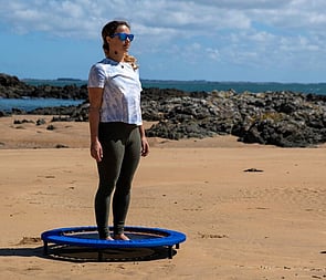 Woman health-bouncing on a XenPod Lymphaciser wellness mini-trampoline at the beach