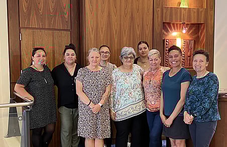 Group of women standing together indoors in front of wooden wall during community workshop or team gathering