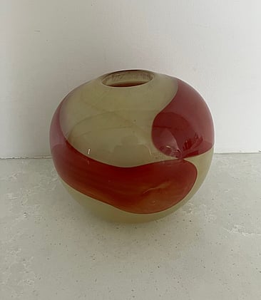 This is an early art glass vase by Ola Höglund and Marie Simberg-Höglund. It is a circular form in a creamy yellow base colour with a red swirl around the centre of the vase.