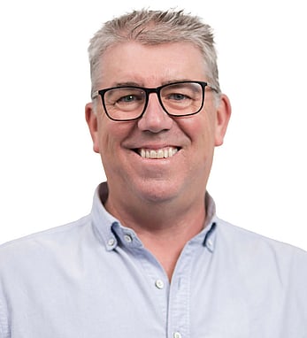 Headshot of Peter, wearing glasses in a light blue shirt, smiling confidently with a plain white background