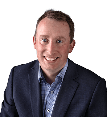 Professional headshot of Calum in a dark blazer and collared shirt, smiling confidently with a plain white background