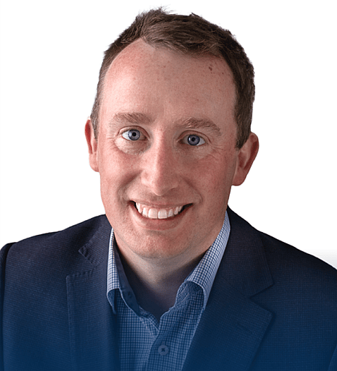 Professional headshot of Calum in a dark blazer and collared shirt, smiling confidently with a plain white background