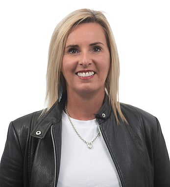 A professional headshot of Adele, smiling and wearing a black leather jacket, with a white background