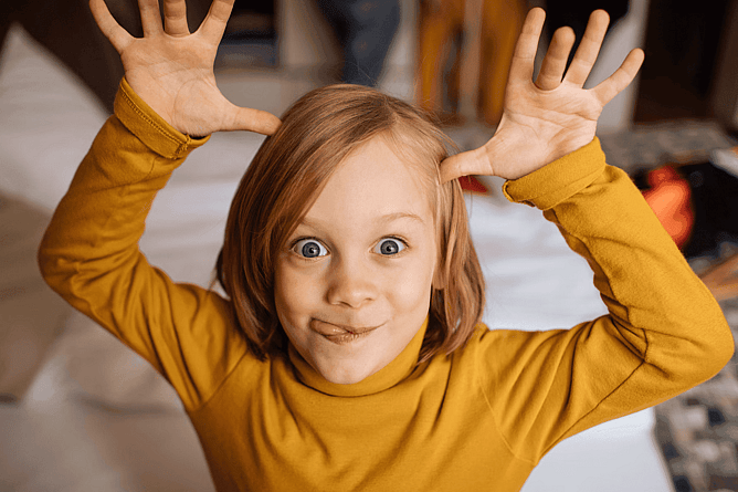 Child pulling a funny face while making a playful expression at home.