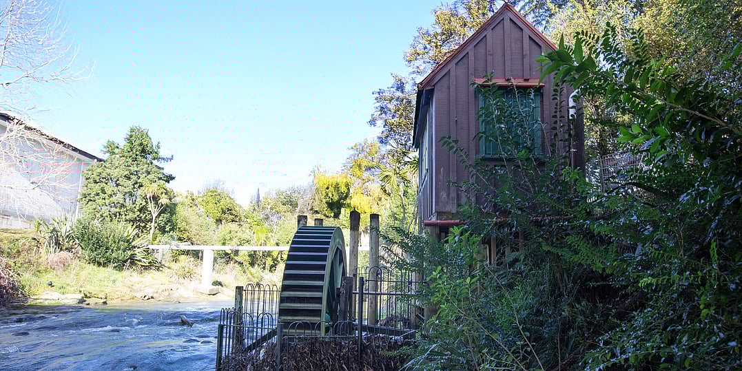 A flowing river with a water wheel next to it and a small wooden building on stilts