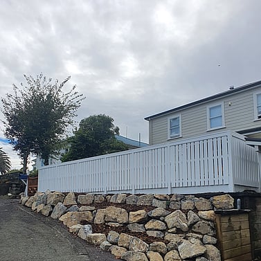 White timber fence above rock retaining wall in residential backyard