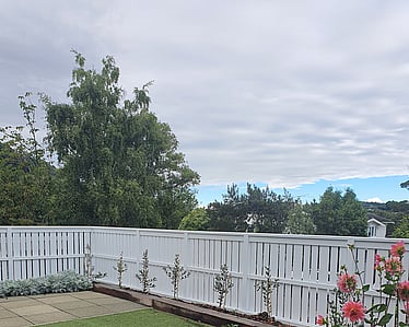 White fence enclosing backyard with artificial lawn and garden beds