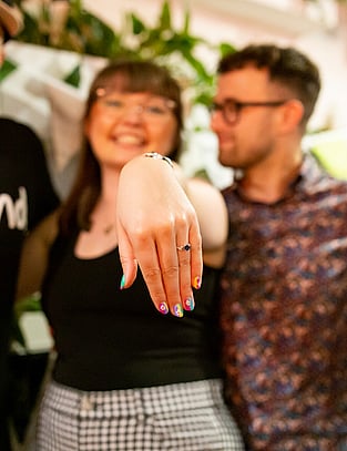 Women poses next to her Fiancee, her hand outstretched showing off her new ring