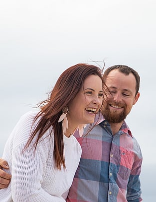 Couple laugh together as they walk down the beach
