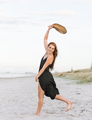 Girl poses on beach holding her hat in the air
