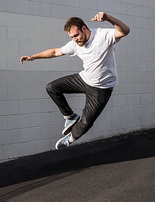 Man poses by jumping In the air and clapping his feet together in industrial car park photoshoot