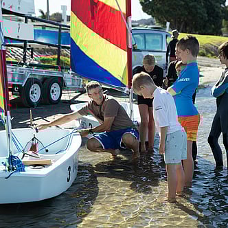 A man showing children how to use a sail boat