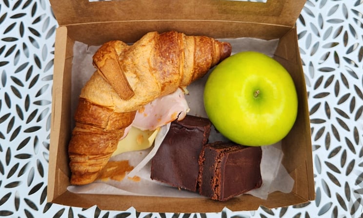 each lunch box. ham and cheese croissant, chocolate brownie and green apple.
