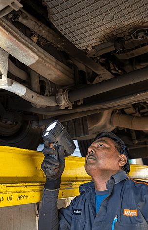 man looking under heavy truck with a flash light inspecting truck for certificate of fitness (cof)