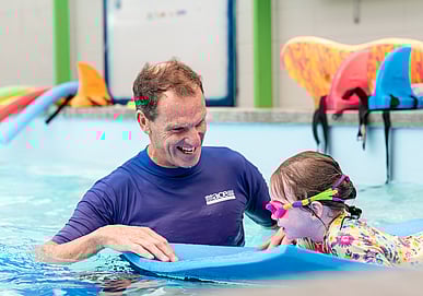 Swimming instructor teaching pre-schooler to kick