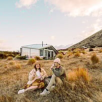 Guests relaxing outside a SkyScape cabin surrounded by tussock and hills