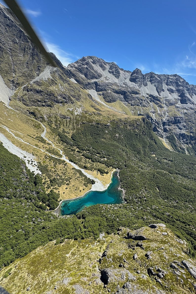 Aerial view of a turquoise volcanic lake surrounded by rugged mountain ranges, capturing the natural beauty found across both islands of New Zealand.