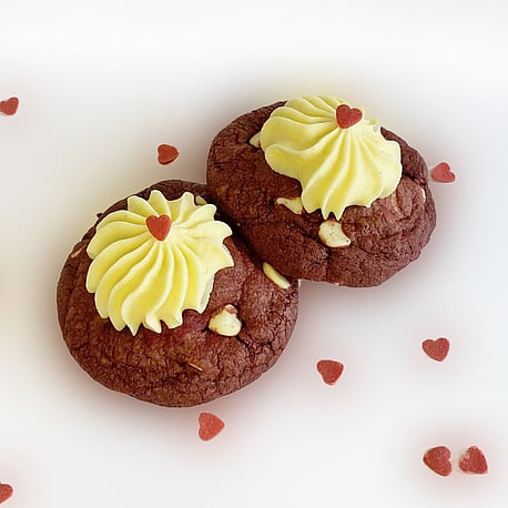 Delicious looking red velvet white chocolate chip cookies filled with cream cheese icing with edible small red heart decorations