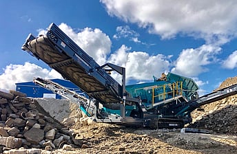 closeup of conveyor arm of Powerscreen Warrior 1800 screening machine working in yard processing waste concrete that has been crushed