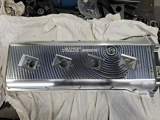 Machined aluminium part with concentric toolpath patterns and two rectangular openings, engraved with “RUSE” logo.