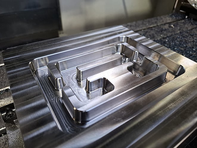 Close-up of CNC-milled aluminium block featuring recessed geometric cavities and sharp internal corners.