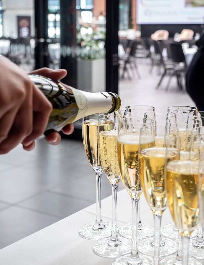 Hands pouring champagne into glasses at charity event in Hamilton, New Zealand.