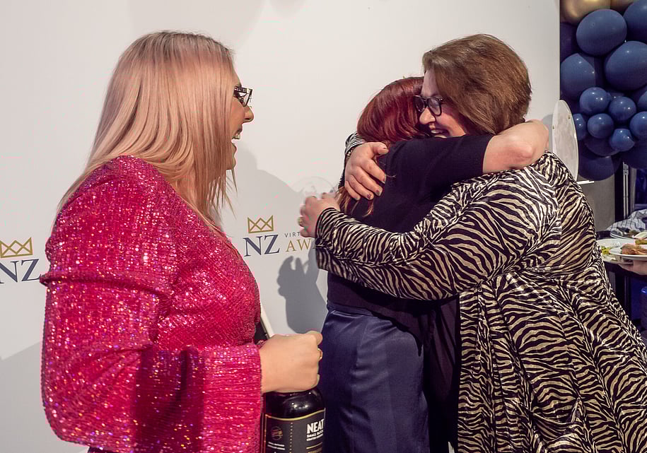 Awards winner and sponsor smiling and hugging in front of the media wall at the Virtual Assistant Awards in Hamilton, New Zealand.