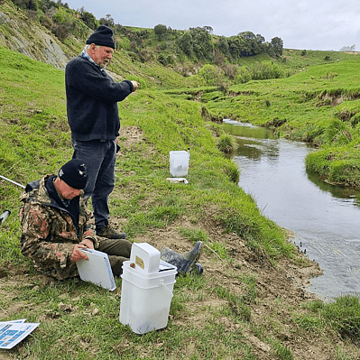 Two people from the Wainuioru catchment group sitting by the river checking water quality results