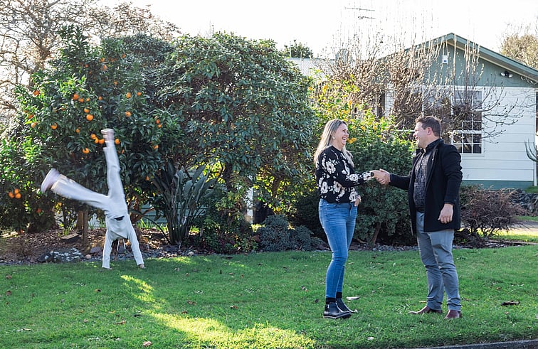Insurance Adviser shaking hands with a young mother, her child doing cartwheels in the background