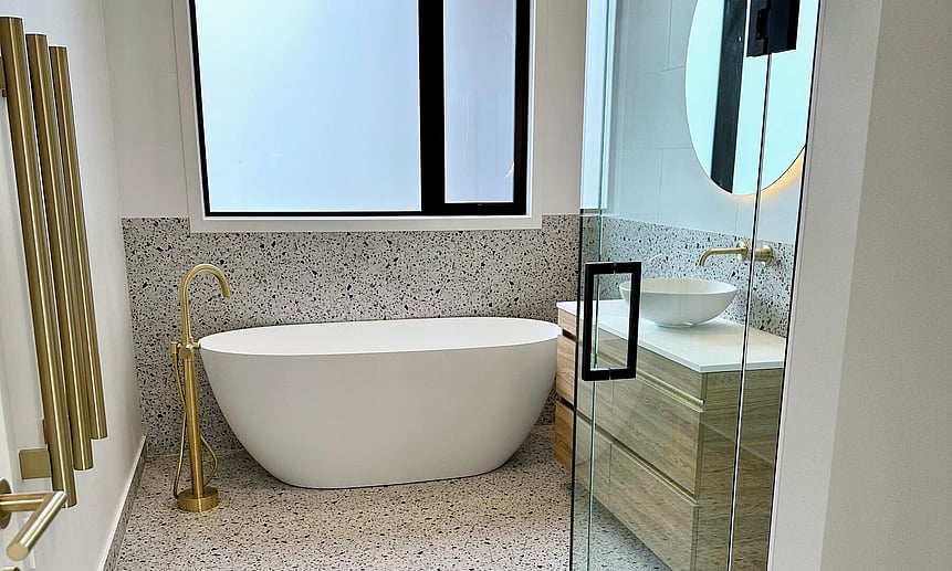 A deep freestanding bath is framed by floor-to-half-height tiled walls that makes for a bespoke bathroom.