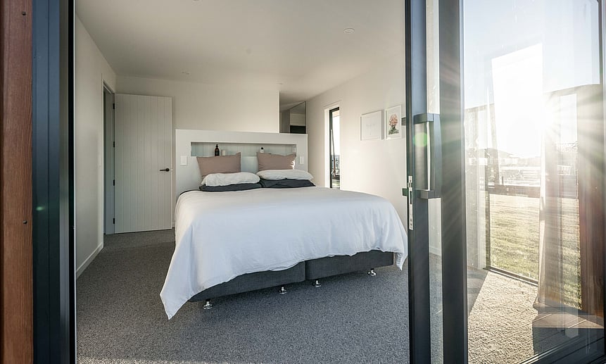This small bedroom features carefully positioned windows that bring the outside in, showcasing this custom-built home.