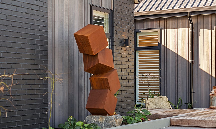 The rustic cube sculpture featured outside the architecturally built house creates unique spaces in this custom home.