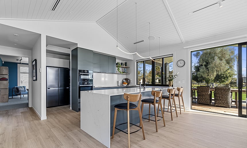 A custom-built modern kitchen with high ceilings features unique white wooden ceiling panels in this award-winning home.