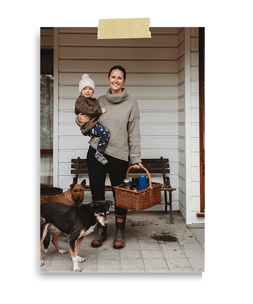Jaz Mathisen holding her child with a basket in her hand and two working dogs at her feet.