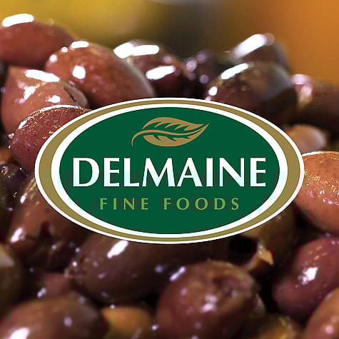 Green and gold Delmaine logo overtop a close up of Spanish olives.