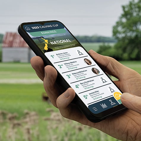 Hand holding mobile phone while using the Elanco Calving Cup app against a rural background.