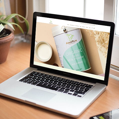 A laptop open on a table showing the AwaRua website with a close up image of AwaRua Organic Skim Milk Powder.