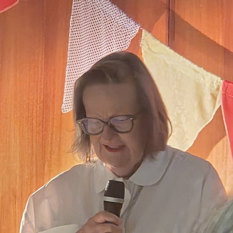 A woman speaking into a handheld mic. Colourful bunting in the background.