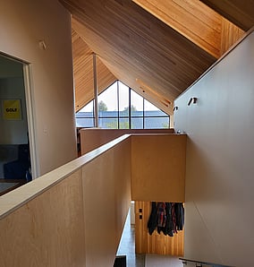 View from timber stair to the concrete-floored entry of an architectural rural home in Matamata with plywood walls, coat cupboard and glazed front door, built by MB Construction.