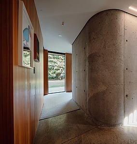 Hallway in an architectural rural home in Matamata with curved concrete wall, timber panelling and views through to the living space, crafted by MB Construction.