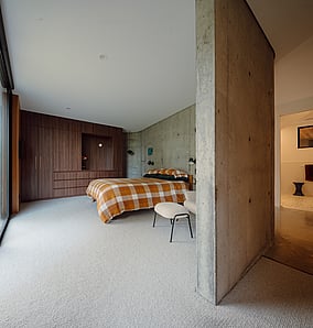 Main bedroom in an architectural rural home in Matamata with concrete feature wall and open link through to the ensuite, designed and built by MB Construction.