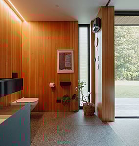 Main ensuite in an architectural rural home in Matamata with timber-lined walls, terrazzo floor and glazed door opening onto a private deck, designed and built by MB Construction.
