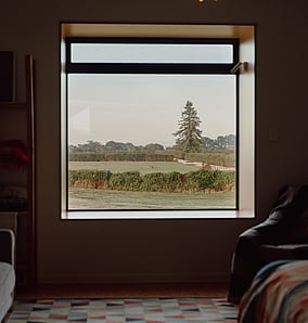 Bedroom in an architectural rural home in Matamata with large window framing rural views across the countryside, built by MB Construction.