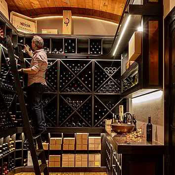 man climbing a ladder and looking at wines in the wine cellar. 